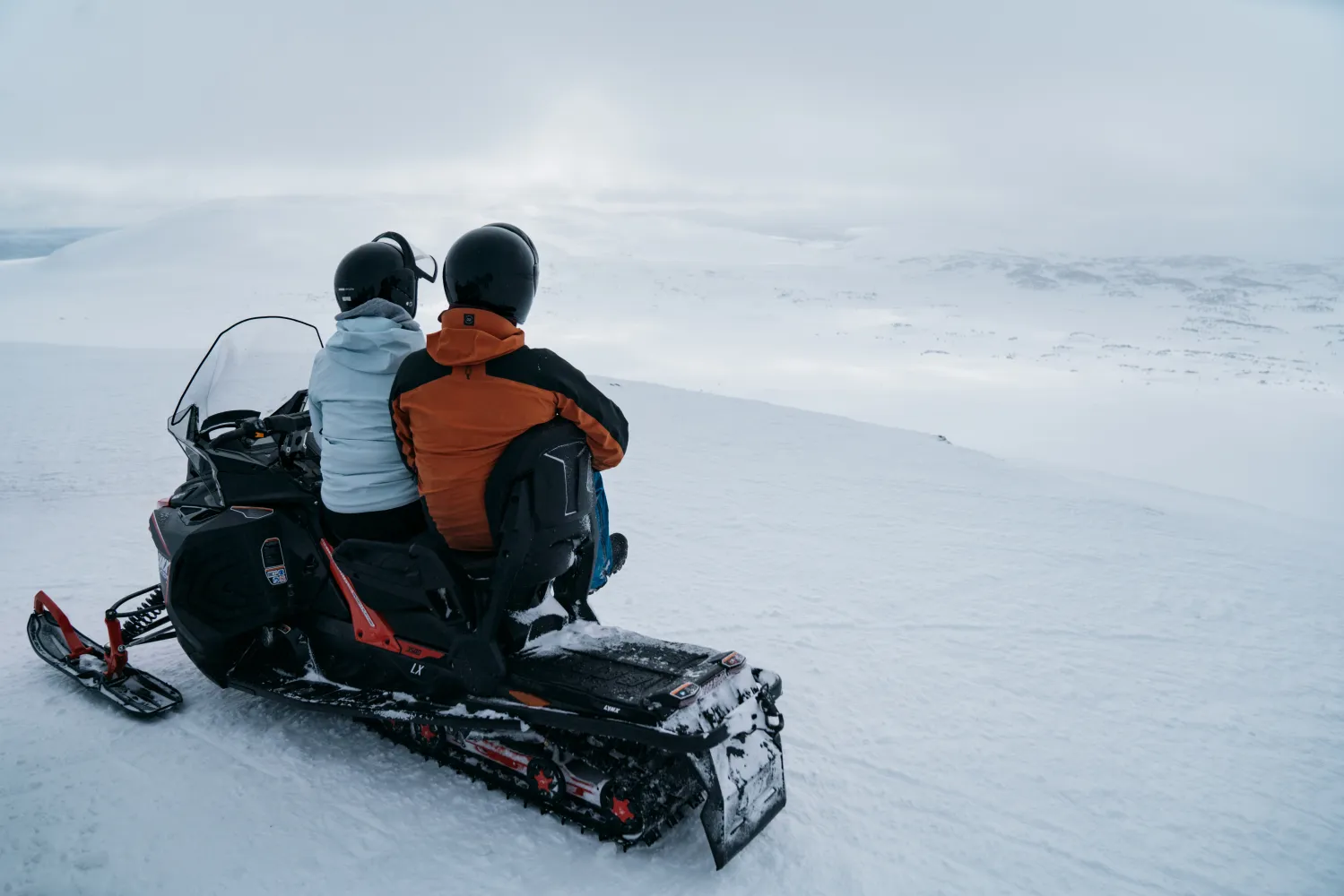 Personer som sitter på en snöskoter i ett snölandskap