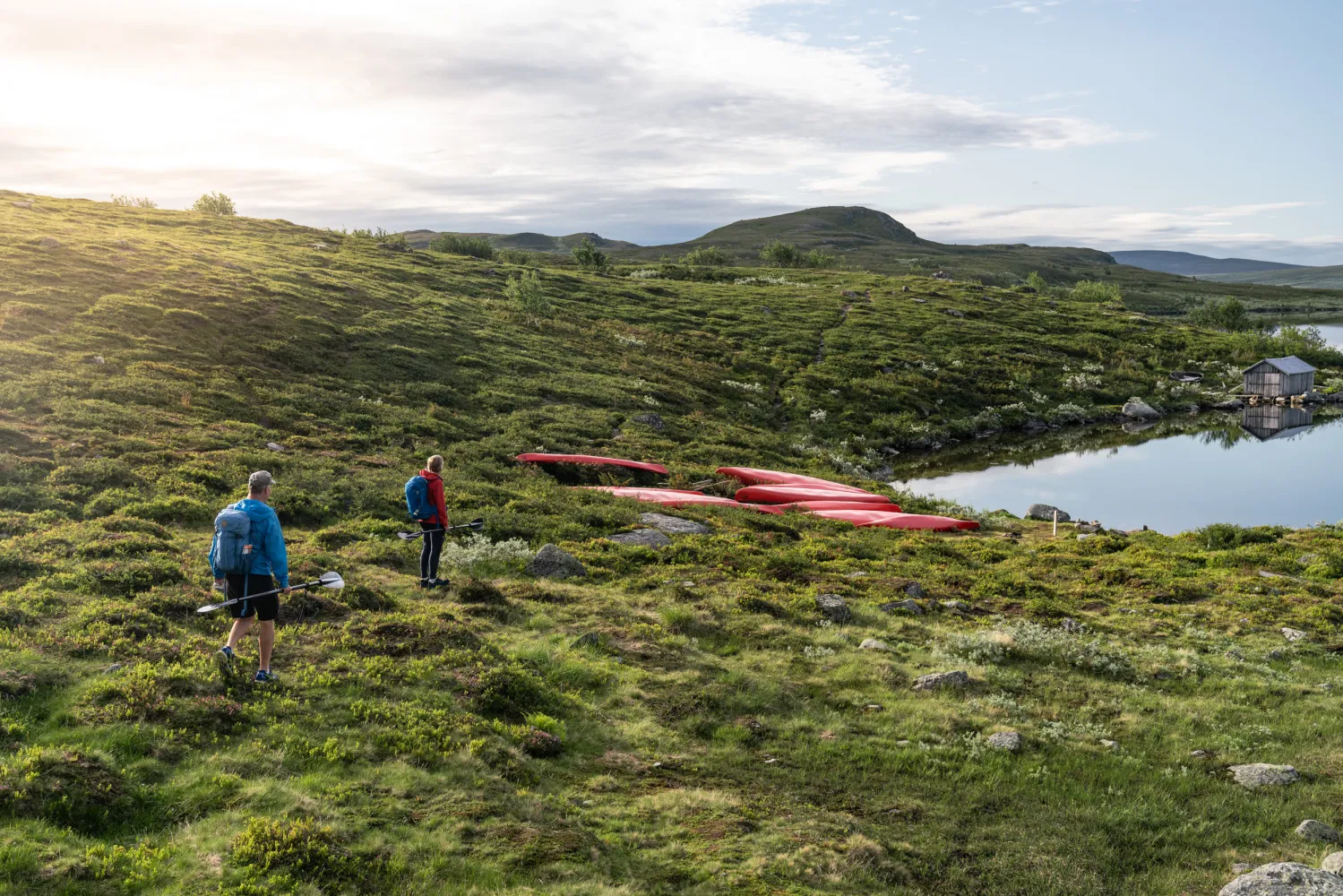 Två personer som står på fjället bredvid en sjö redo att paddla kayak
