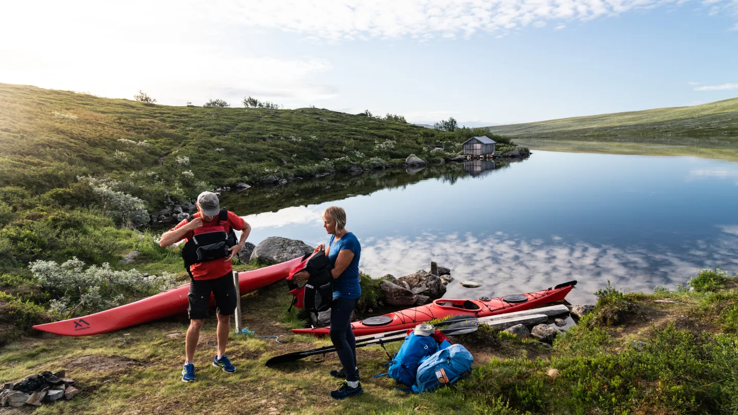 Två personer som förbereder sig på att paddla kayak i en sjö på fjället