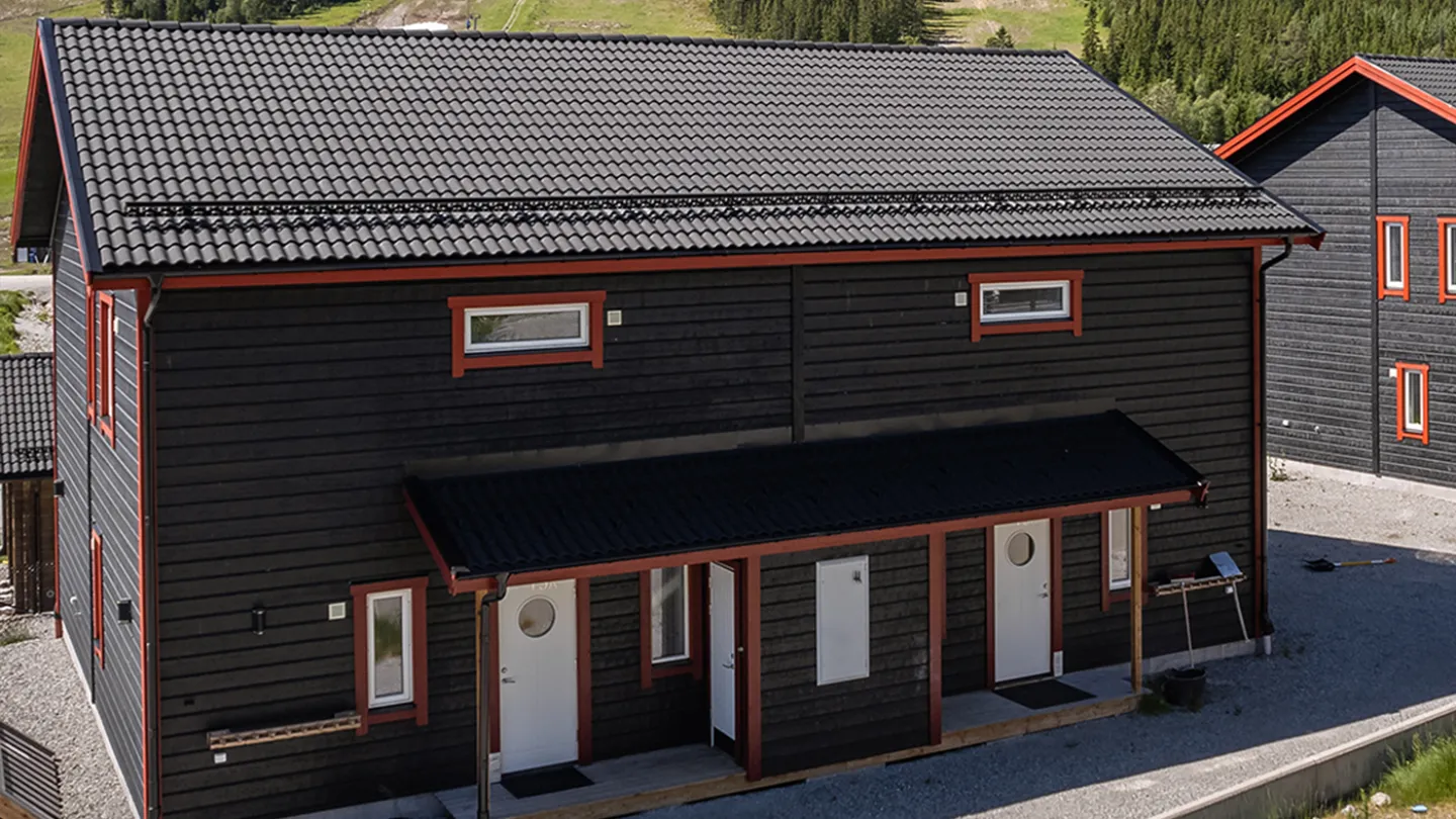 ett svart hus med vita dörrar och ett gräsbevuxet fält